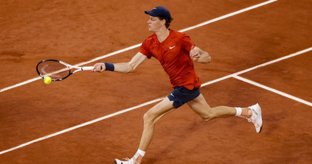 annik Sinner, wearing a red shirt and navy shorts, lunges forward on a red clay court to hit a forehand return with his racquet. Jannik Sinner Rome comeback